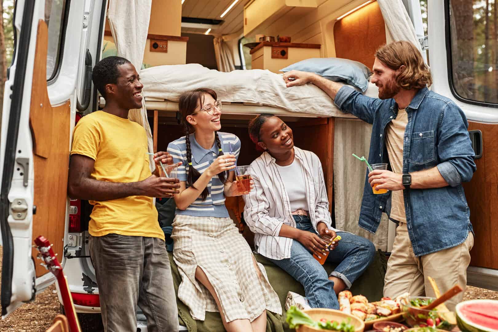 Group of friends drinking cocktails and talking to each other during camping on motorhome